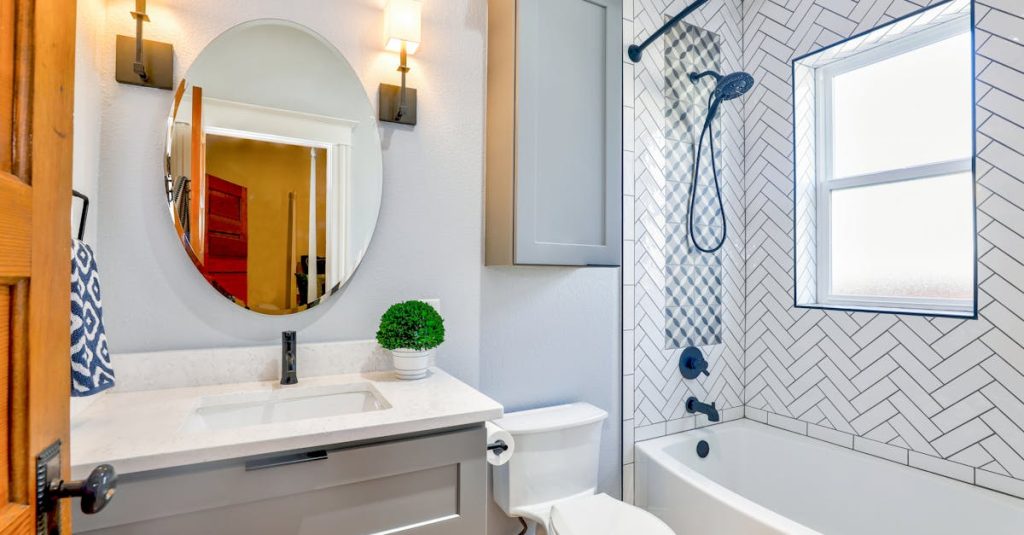 Elegant modern bathroom featuring chevron tiles, oval mirror, and sleek fixtures for a contemporary look.
