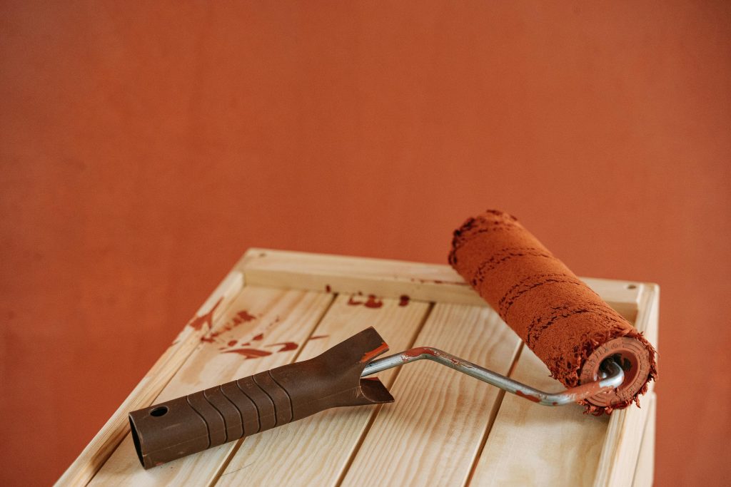 A paint roller with rustic brown paint on a wooden surface against an earthy wall.