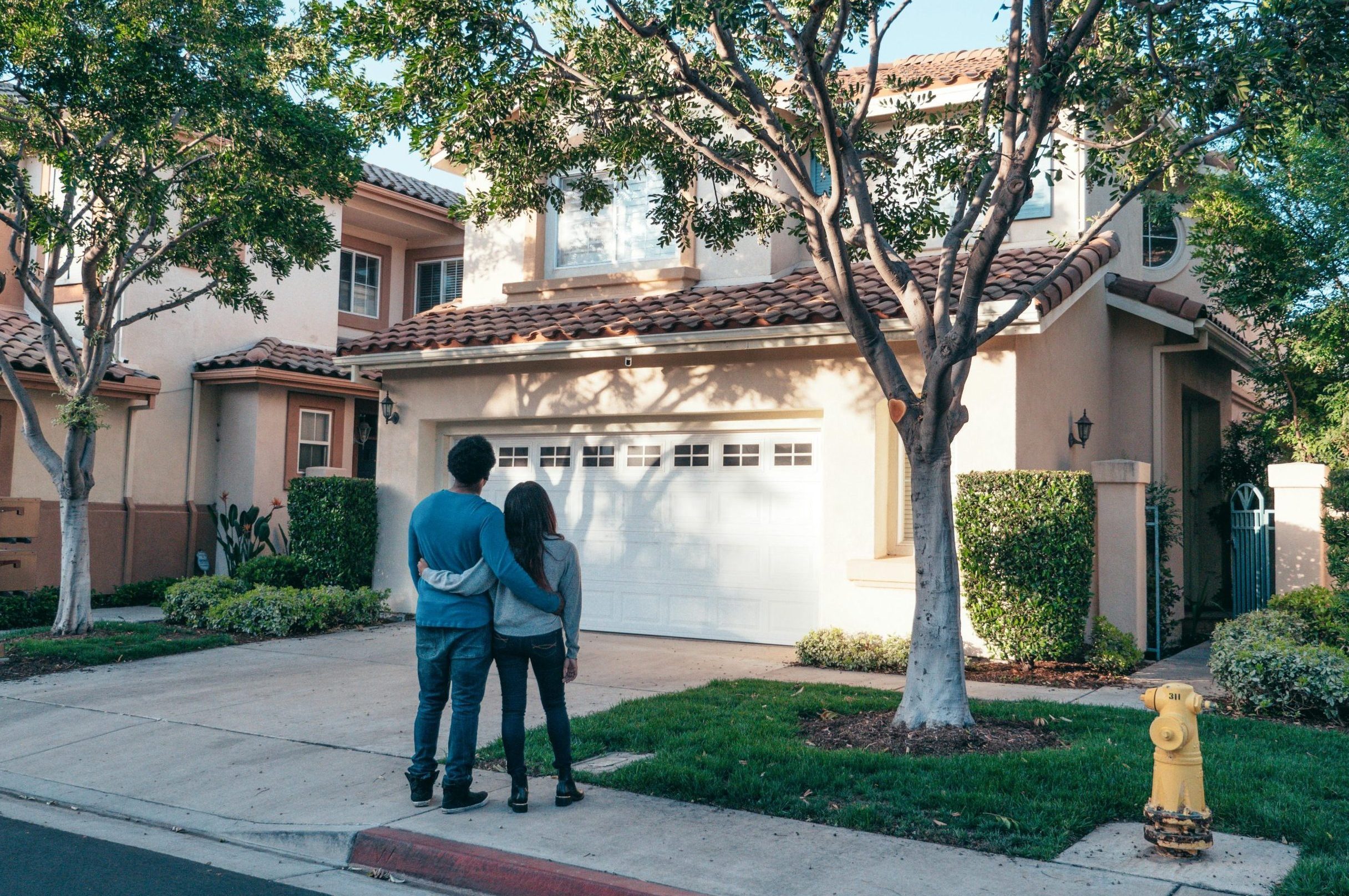 Couple hugging outside their newly purchased suburban home, showcasing togetherness and new beginnings.