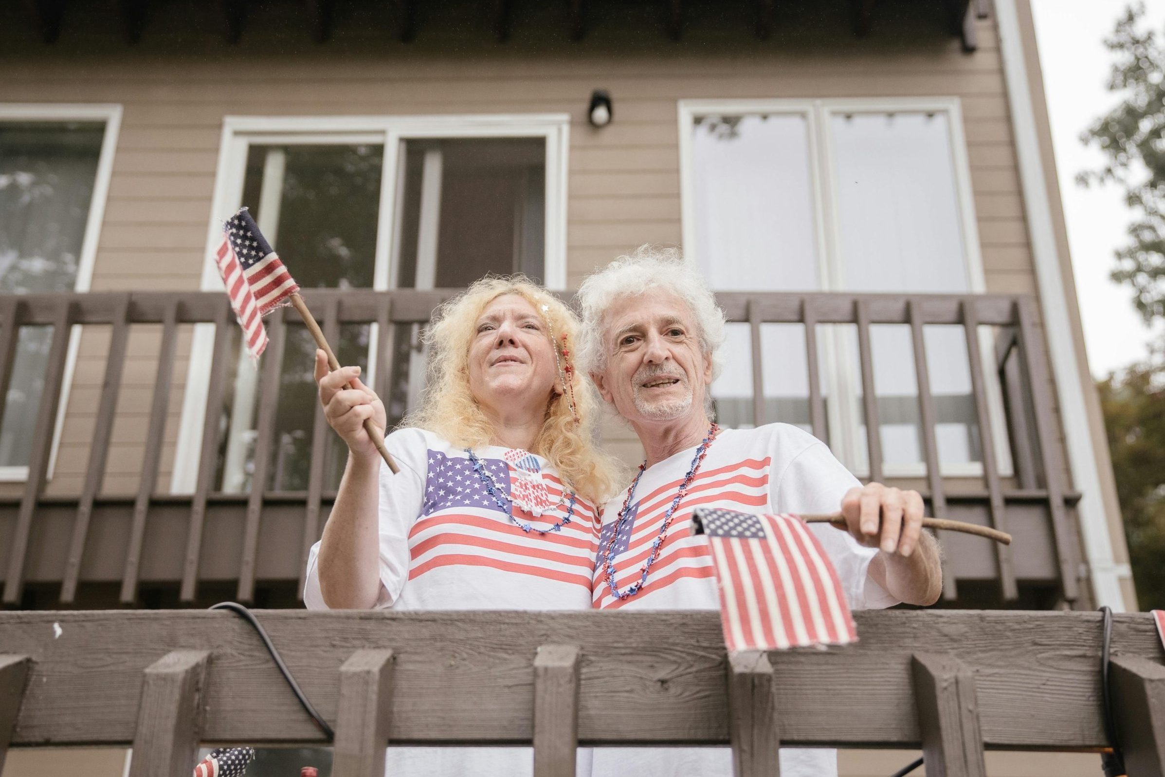 Senior couple on balcony with US flags, enjoying a festive celebration outdoors.