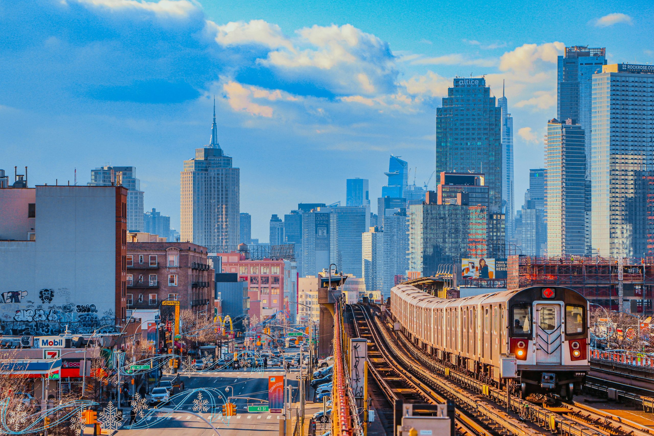 Dynamic view of New York City's skyline with a subway train in foreground, under blue sky.